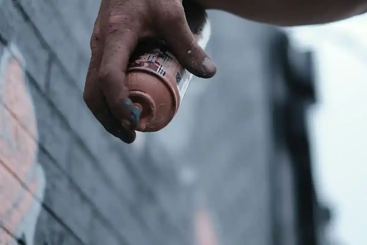 Close-up of a mural artist's hand gripping a spray can against a painted brick wall